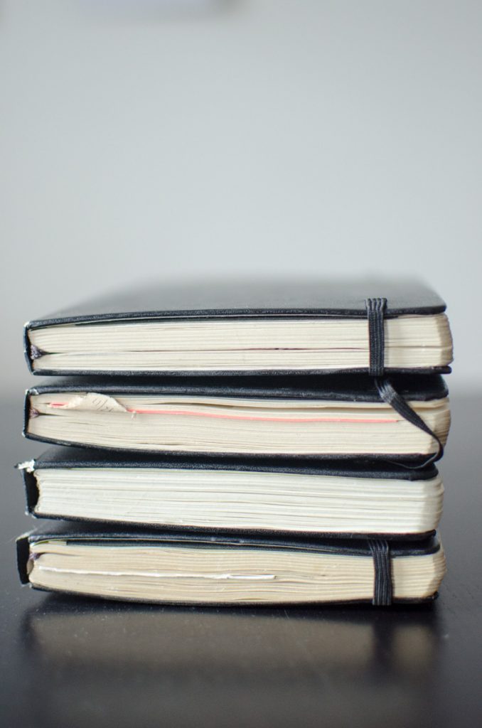 A stack of four well-used black notebooks held closed with elastic bands